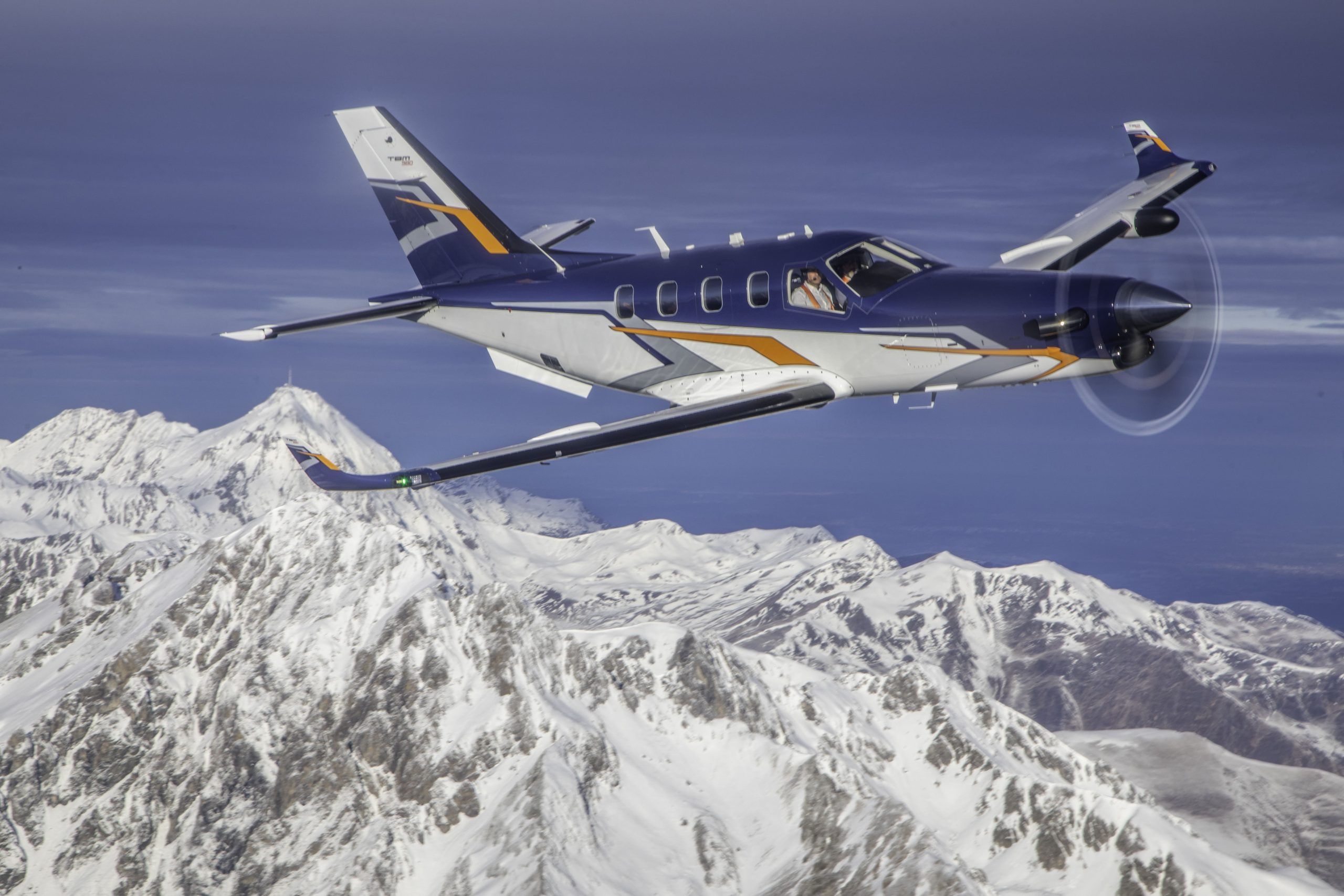 A TBM turboprop in flight over snow-covered mountains